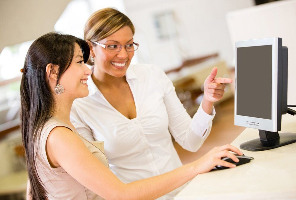 woman helping another woman find something in a computer