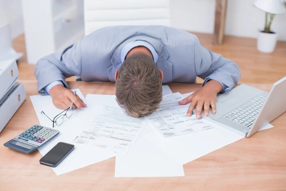 business man with head on desk of papers