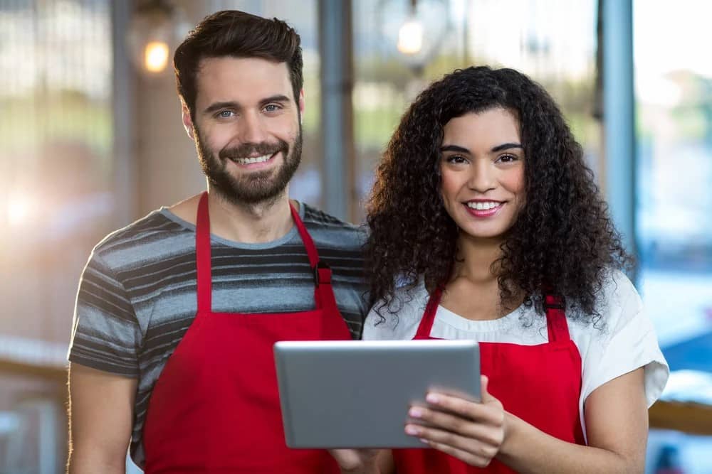 Portrait of smiling waiter and waitress using digital tablet at counter in cafe