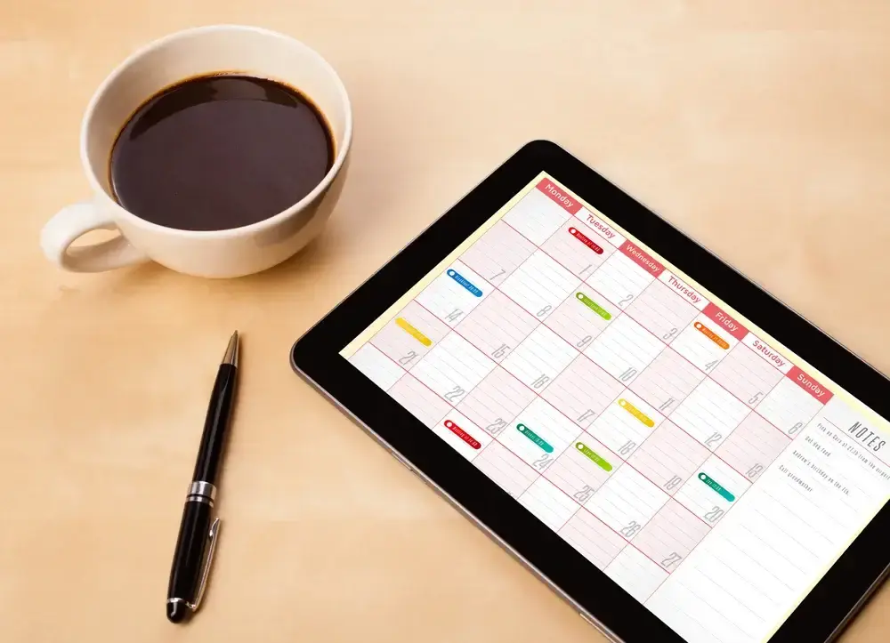 workplace with tablet showing calendar, cup of coffee and a pen